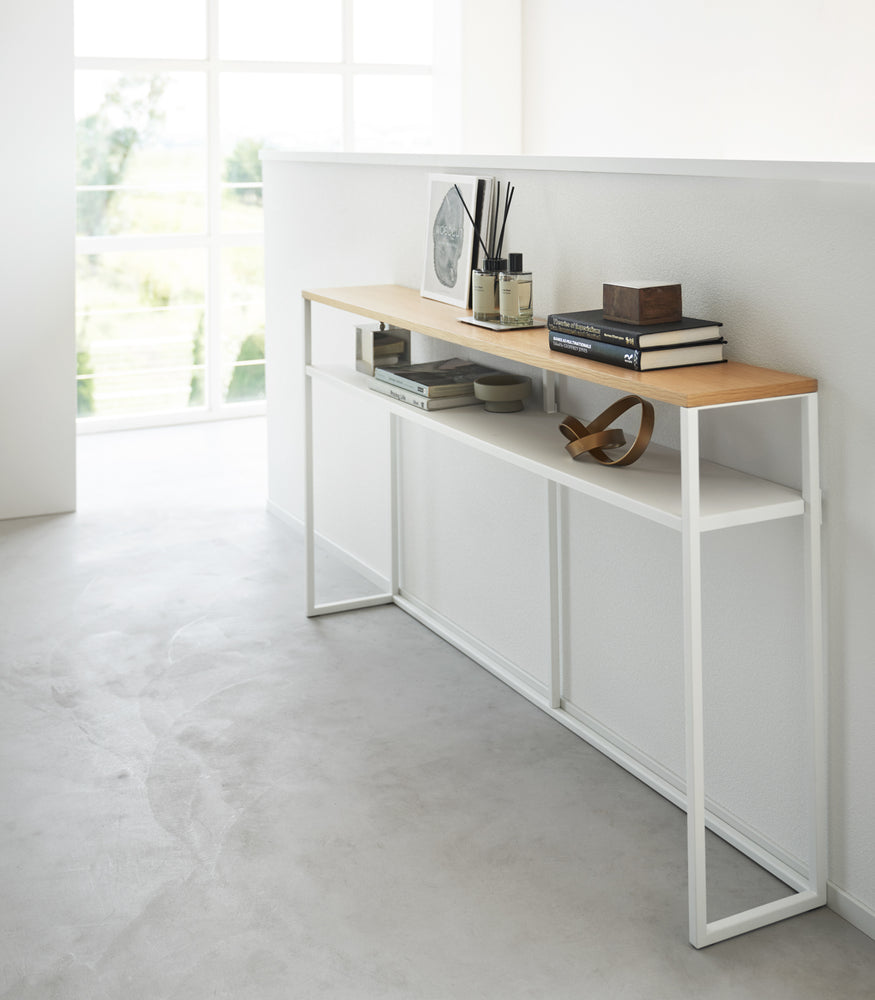 View 17 - White Yamazaki Home Long Console Table - Shelf against a wall with books and decorations on it