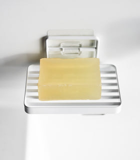 Yamazaki Home's black Traceless Adhesive Soap Tray mounted on a white wall, holding a bar of yellow soap, showcasing minimal design. view 3