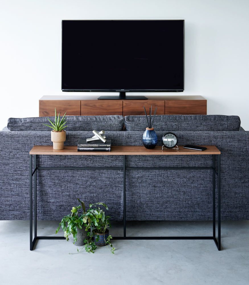 View 12 - Straight view of the Long Console Table by Yamazaki Home in black with decorative items placed behind a gray couch in a living room.