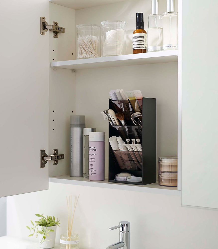View 5 - An angled view of an opened white medicine cabinet. Sunlight is focused on the right upper corner. The top half of the cabinet holds face serums and two clear containers with cotton swabs and rounds.