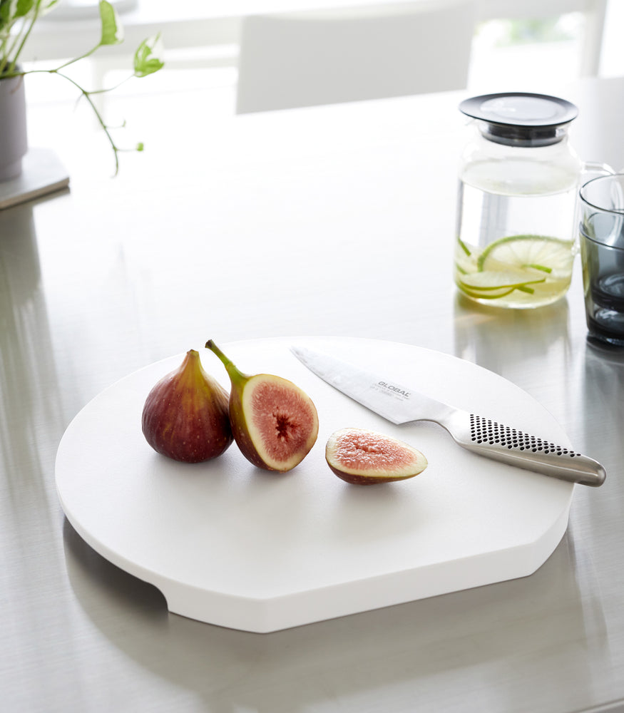 View 8 - A white Yamazaki Round Magnetic Cutting Board with a fig and knife on it on a countertop.