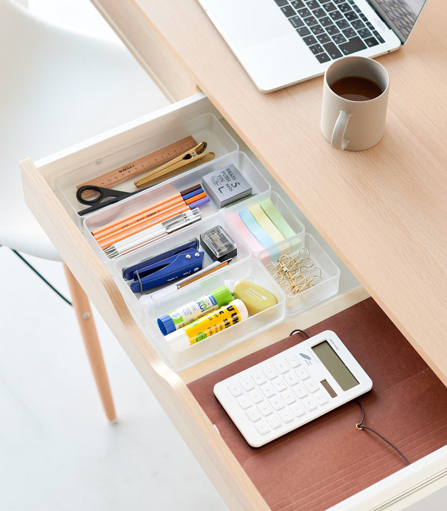 View 35 - Three different sizes of stackable clear organizers—small, medium, and large—are neatly placed in a desk drawer. Made from transparent material, they accommodate stationery items like pens, paper clips, and sticky notes, showcasing their clarity and stackability.