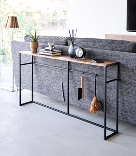Diagonal view of the Long Console Table by Yamazaki Home in black placed behind a gray couch in a living room. view 10