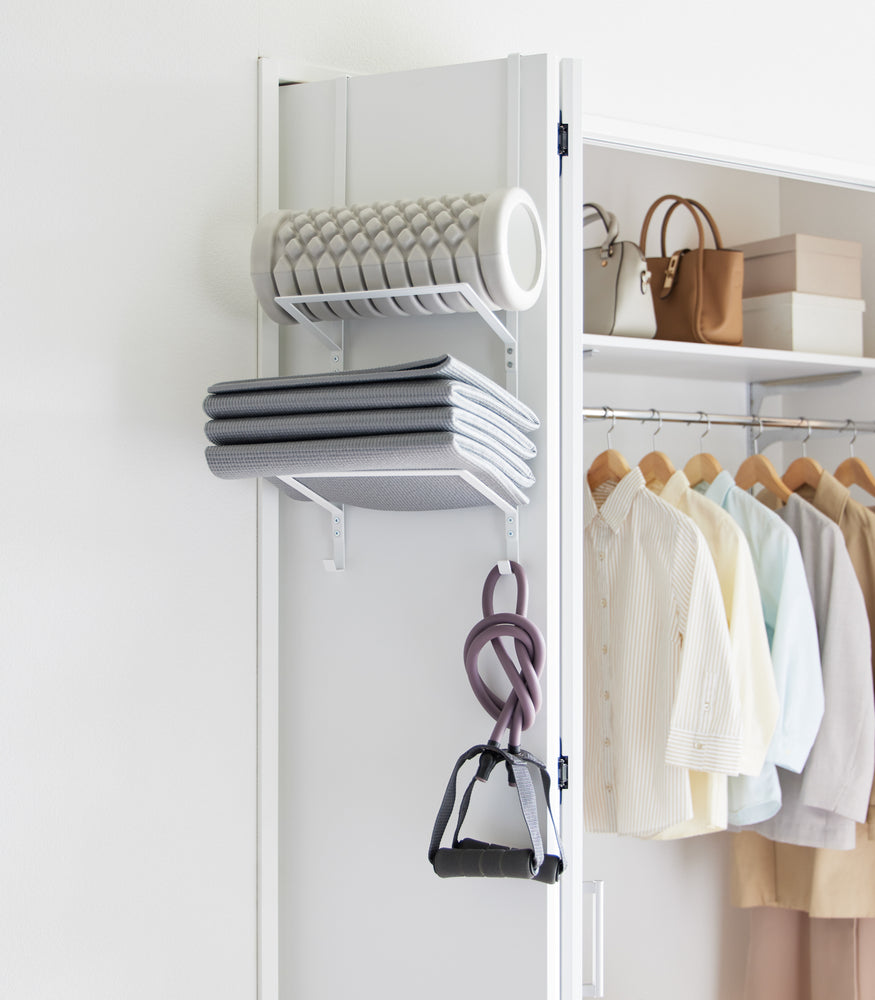 View 3 - Over-the-Door Fitness Equipment Hanger by Yamazaki Home in white hanging on an accordion closet door storing various exercise items.