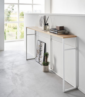 Diagonal view of the Long Console Table by Yamazaki Home in white placed by a wall with decorative items. view 3