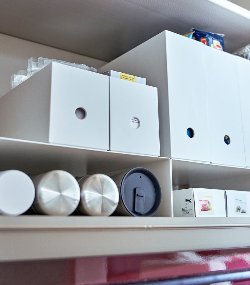 White Yamazaki Home Shelf Risers in a cabinet containing water bottles and food wrap boxes