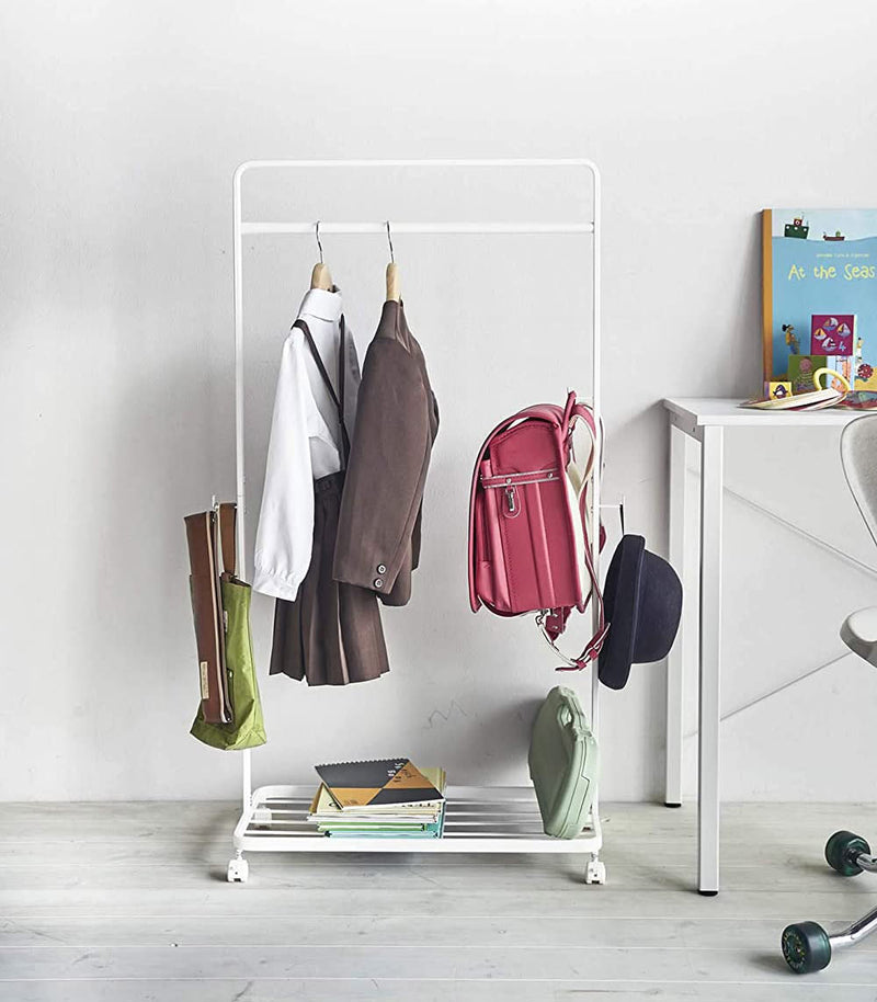 Front view of white Rolling Coat Rack holding school uniforms, backpack and school supplies by Yamazaki Home.