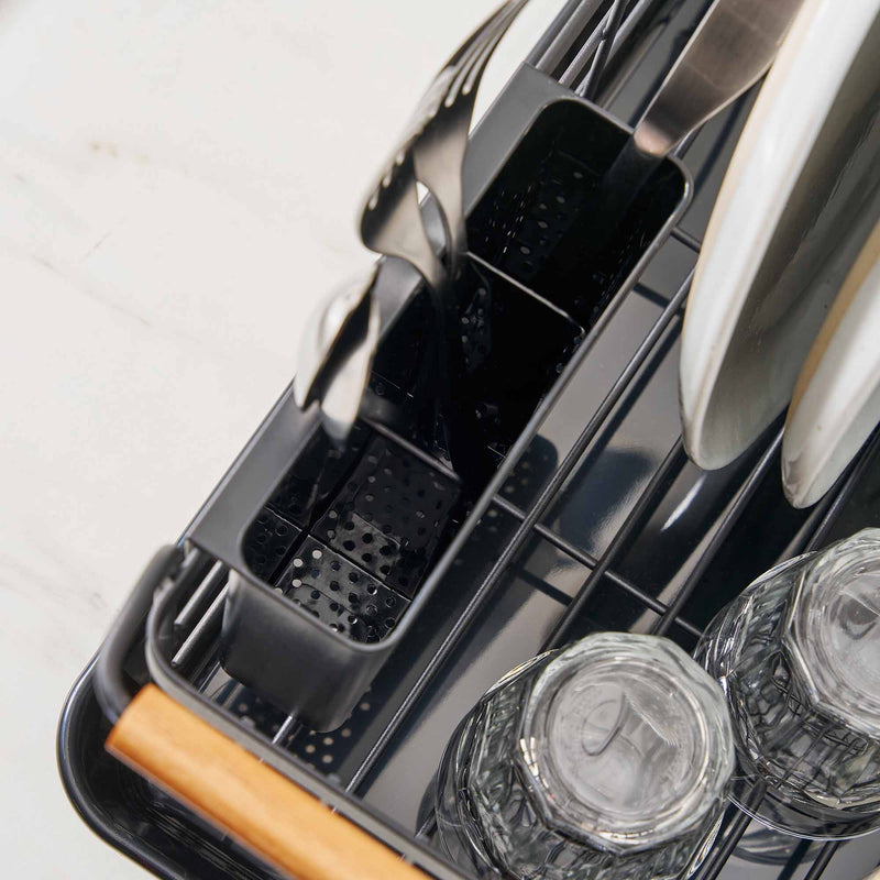 Removable utensil holder holding three forks on a black dish drying rack with wood handles in a modern kitchen.
