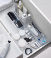 Four different sizes of stackable clear organizers—small, medium, large, and deep—are neatly placed in a bathroom drawer. Made from transparent material, they accommodate items like brushes and sanitary products, showcasing their clarity and stackability.
