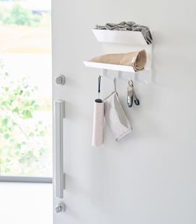 Magnetic Entryway Rack by Yamazaki Home in white mounted on a door holding various entryway items including a hat and keys. view 3