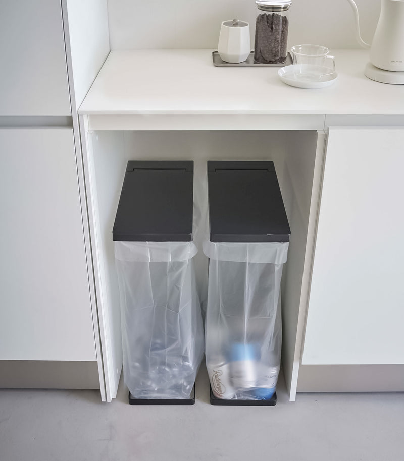 Two Black Yamazaki Home Lidded Garbage Bag Holder under a shelf