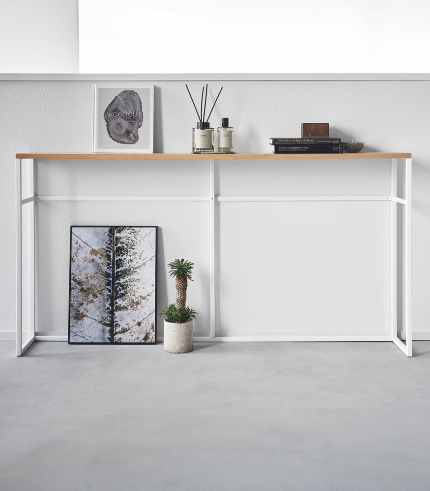 View 8 - Straight view of the Long Console Table by Yamazaki Home in white placed along a wall with decorative items.