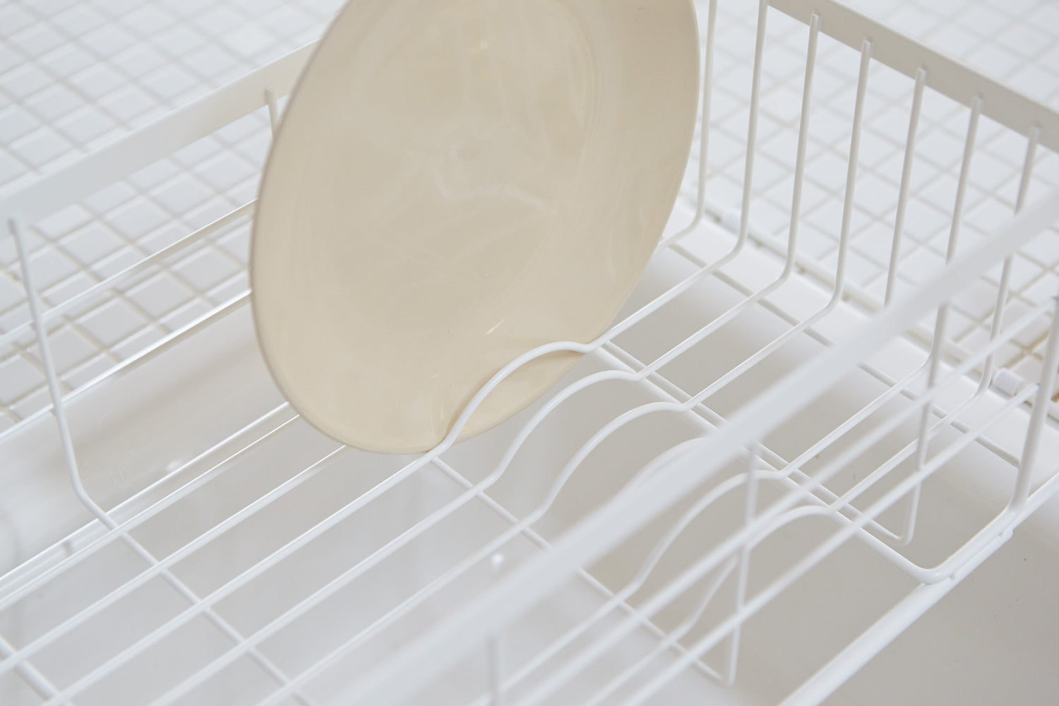 View 6 - Close up view of white Over-the-Sink Expandable Dish Drying Rack holding plate in kitchen by Yamazaki Home.