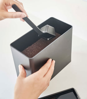 Scooping out coffee from black Yamazaki Home coffee storage container with measuring spoon view 13