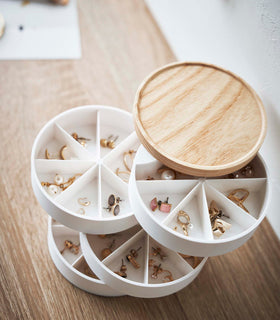 A four-tier swivel accessory organizer with a light-colored wooden lid is displayed in an all-white room. The accessory holder’s tiers and lid are swiveled opened so the inside contents can be seen, each tier has seven individual compartments formed in a pie shape. Each individual compartment of the tiers holds a pair of earrings. view 10