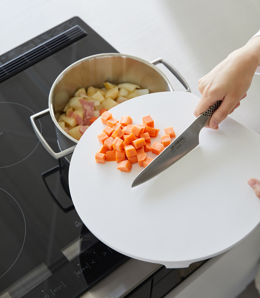 View 6 - A white Yamazaki Round Magnetic Cutting Board being used to cut carrots.