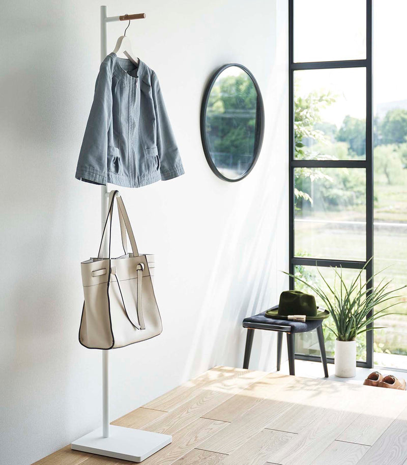 Side view of white Yamazaki Coat Rack with a purse and jacket hanging on it in an entryway