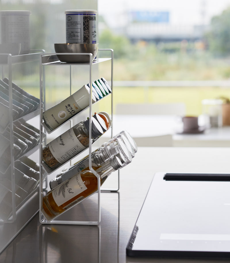 Side view of a White Four-Tier Slim Spice Rack by Yamazaki Home neatly organized with spices and oil bottles on a light kitchen countertop.