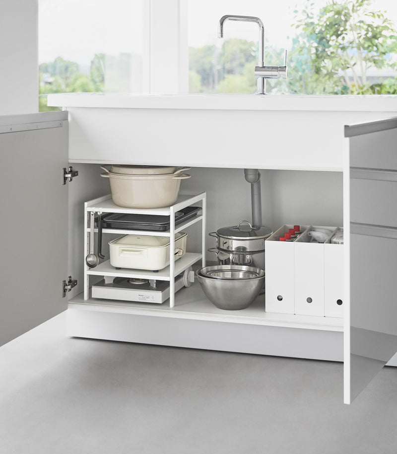 Yamazaki Home White Three-Tier Cabinet Storage Rack holding pot and pans under the sink.