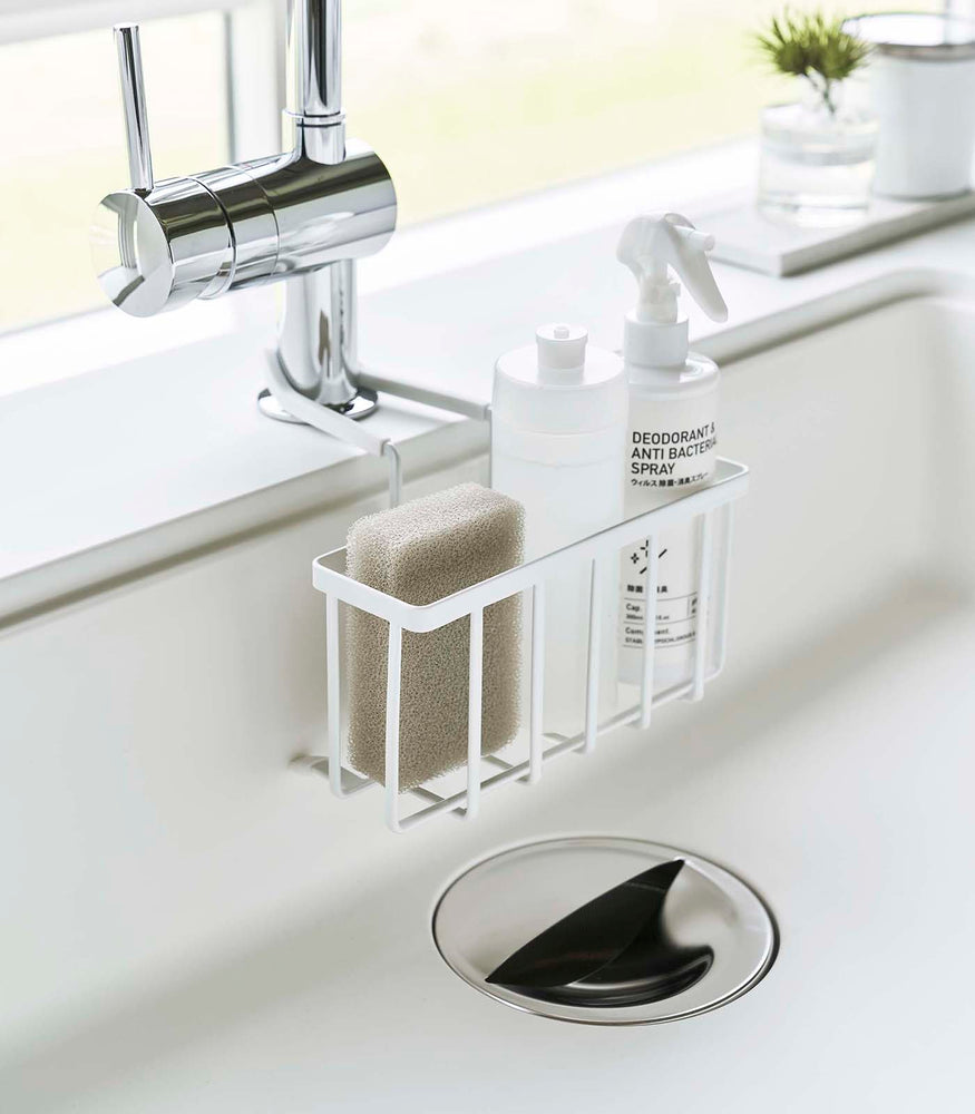 View 15 - White Faucet-Hanging Sponge Caddy attached to the kitchen sink faucet and holding sponges and cleaning supplies by Yamazaki Home.