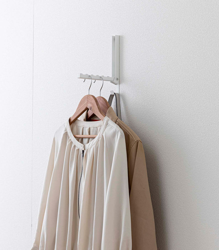 View 17 - White Yamazaki Home Folding Over-The-Door Hanger mounted with multiple jackets hung