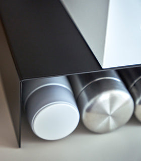 Close up of black Yamazaki Home Shelf Risers in a cabinet with water bottles beneath view 11