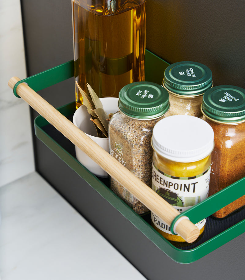 Close up top-down view of Forest Green Yamazaki Home Magnetic Storage Caddy with oil, herbs and spices stored attached to a refridgerator