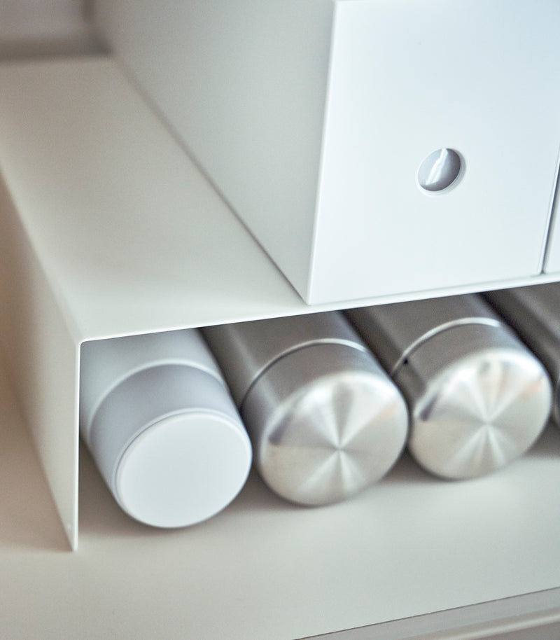Close up of white Yamazaki Home Shelf Risers in a cabinet with water bottles