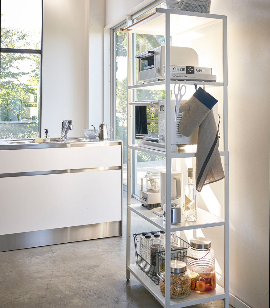 View 21 - Tall white five-tier steel storage rack with a decorative wood accent bar on top shelf and white adjustable hooks on sides.