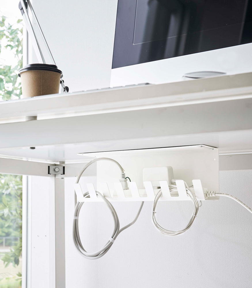 View 3 - Under-Desk Cable Organizer in white by Yamazaki Home mounted under a desk holding cables.