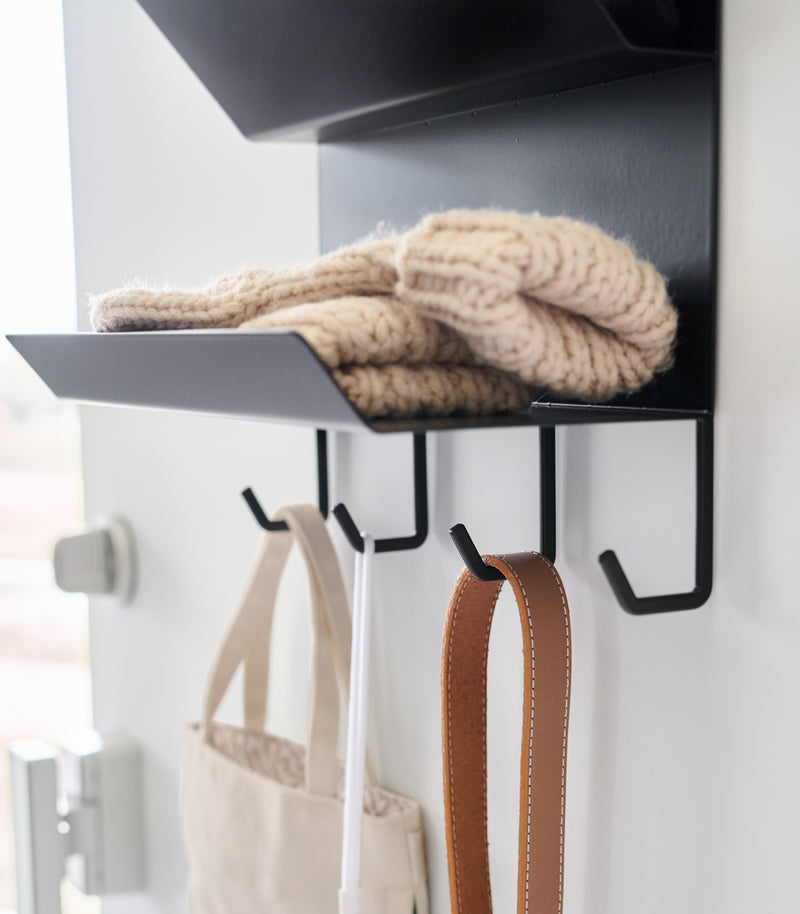 Close-up of the hooks on the Magnetic Entryway Rack by Yamazaki Home in black. Various entryway items are stored on the rack including gloves and a dog leash.