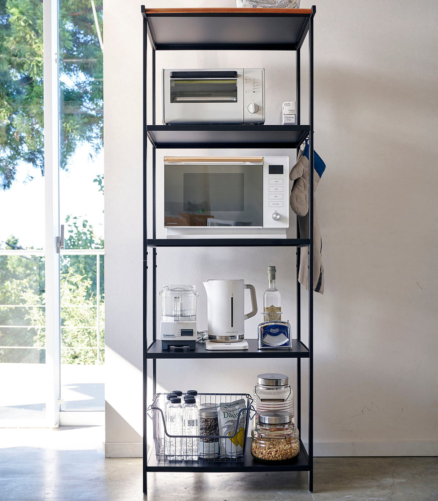 View 29 - Tall black five-tier steel storage rack with a decorative wood accent bar on top shelf and adjustable hooks on sides.
