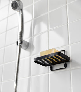 Yamazaki Home's black Traceless Adhesive Soap Tray in a shower, holding a bar of soap next to a silver shower hose on tiled wall. view 13