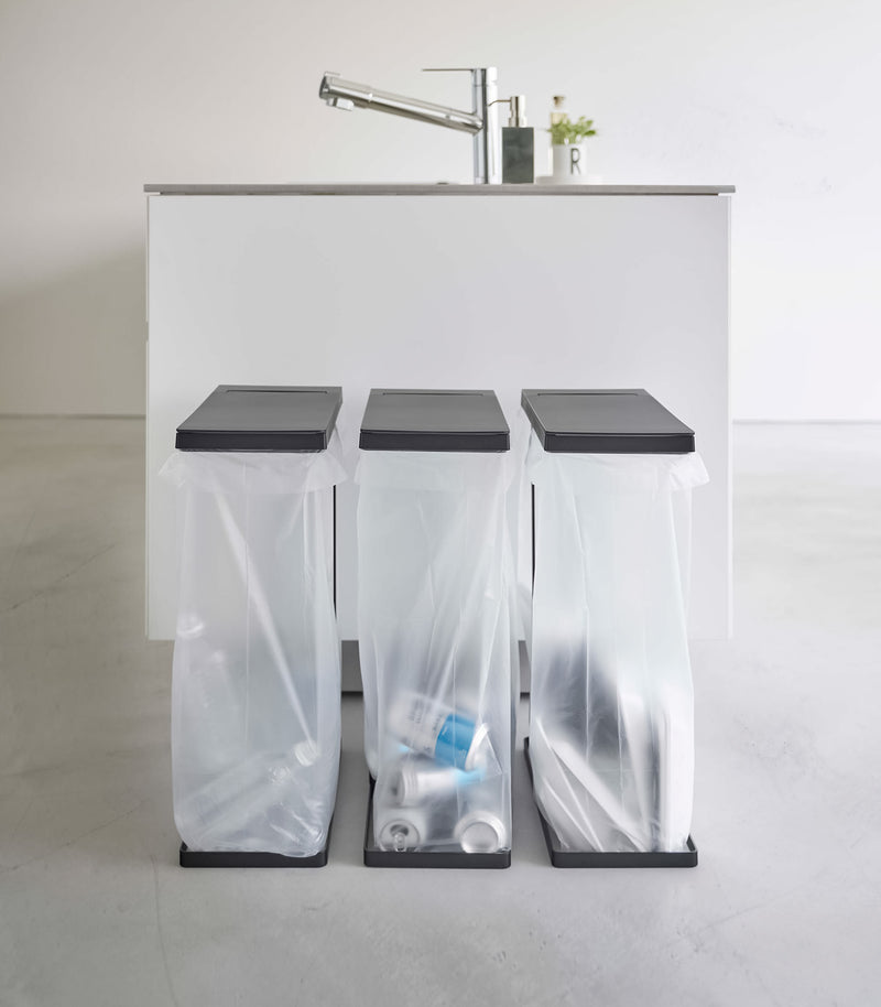 Three Black Yamazaki Home Lidded Garbage Bag Holder filled with different recyclables