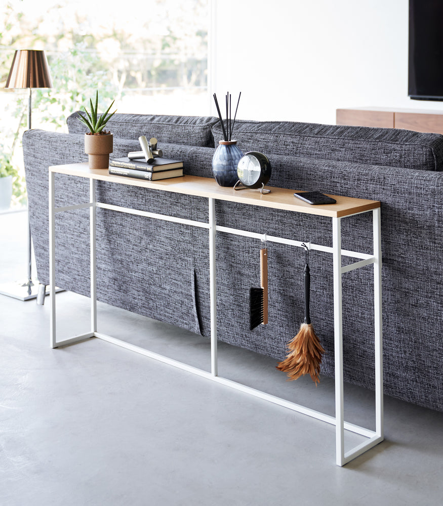 View 2 - Diagonal view of the Long Console Table by Yamazaki Home in white placed behind a gray couch in a living room.