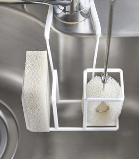 Close up of white Steel Yamazaki Home Faucet-Hanging Sponge & Brush Holder storing a brush and a sponge view 4
