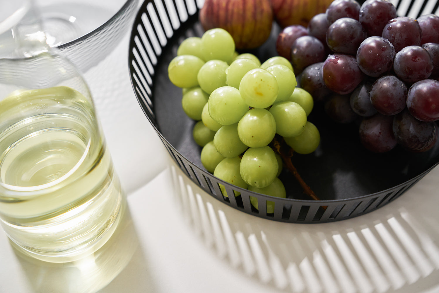 View 12 - Close up aerial view of black Fruit Basket holding grapes on white tabletop by Yamazaki Home.