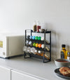 Front view of Black Four-Tier Slim Spice Rack by Yamazaki Home in a well-lit kitchen, equipped with a variety of spices and essentials.