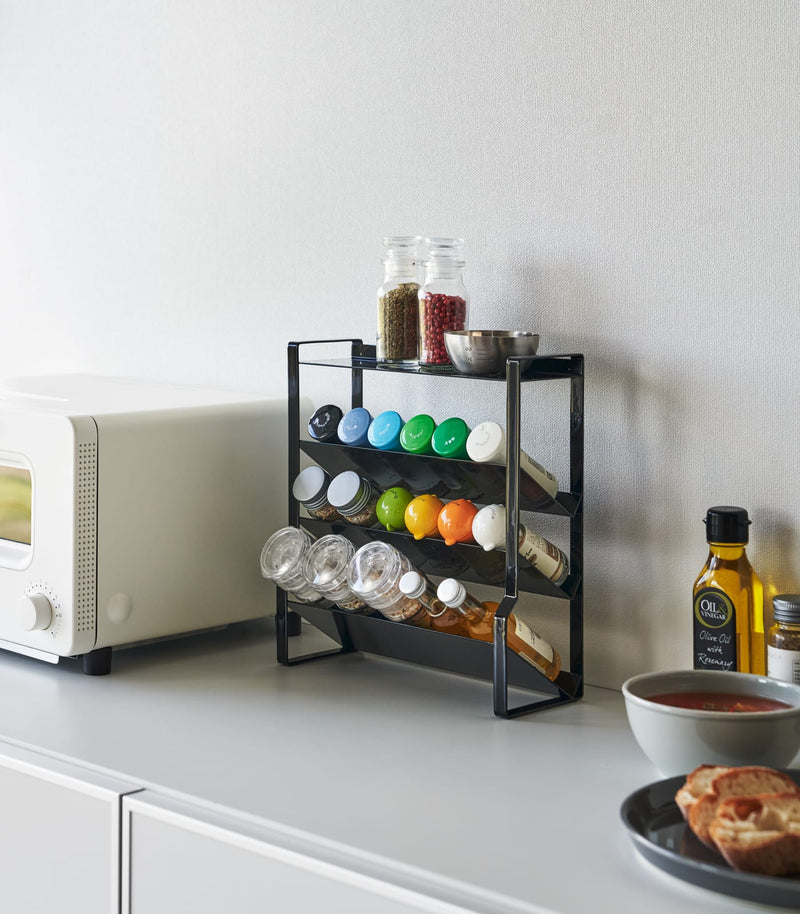 Front view of Black Four-Tier Slim Spice Rack by Yamazaki Home in a well-lit kitchen, equipped with a variety of spices and essentials.