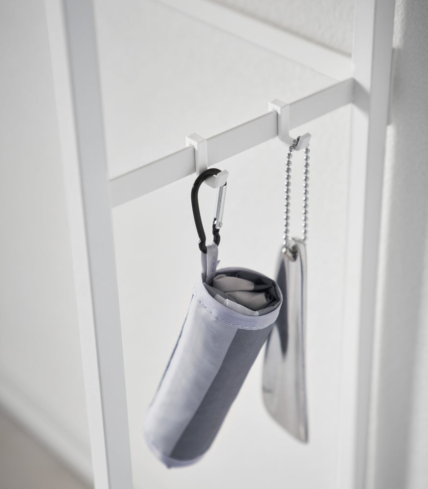 View 7 - A folding umbrella and shoe horn hanging form the side hooks on the Long Console Table by Yamazaki Home in white.