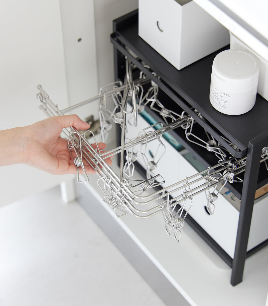 View 15 - Somone is taking out a drying hanger with clips from Yamazaki Home Black Three-Tier Cabinet Storage Rack.