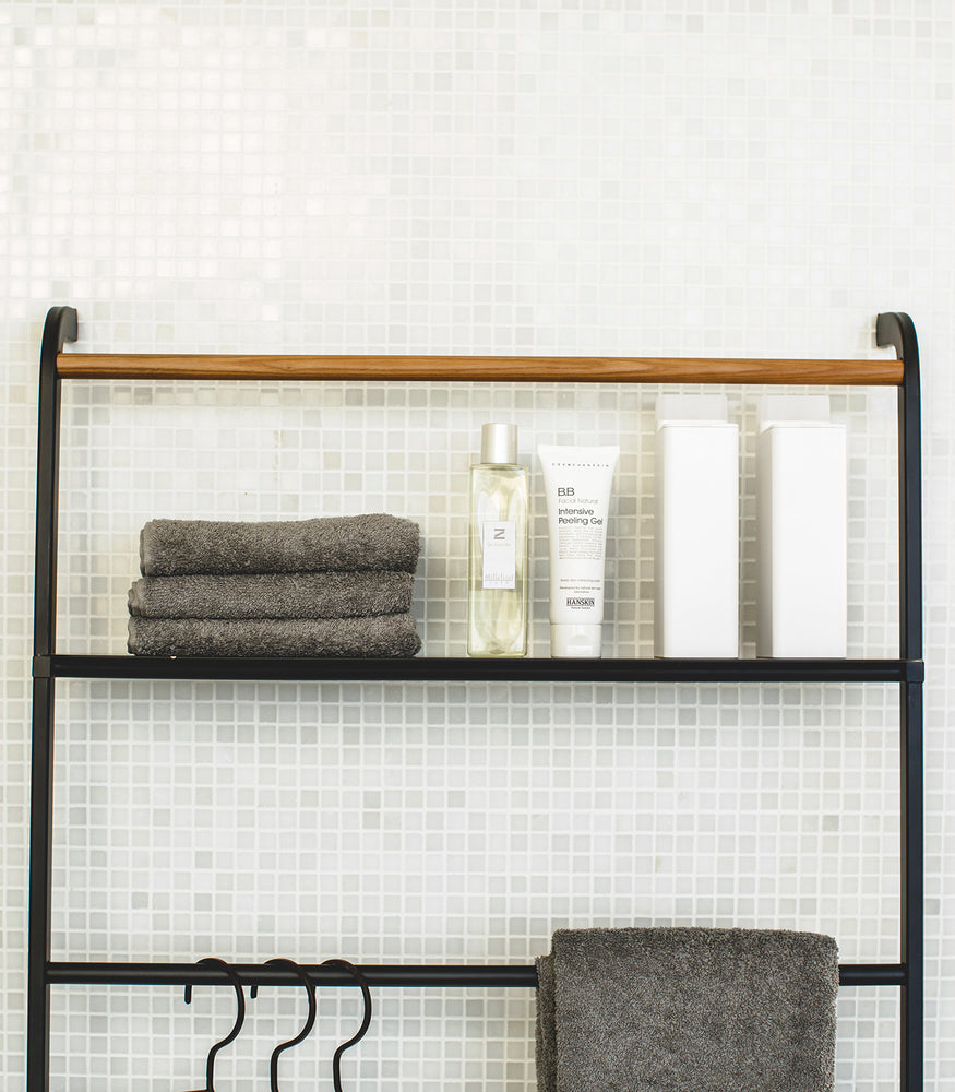 View 22 - Close up front view of black Leaning Ladder Rack with Shelf holding towels and skin care products in bathroom by Yamazaki Home.