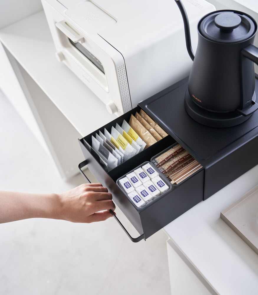 View 13 - Someone is holding a handle of Yamazaki Home Black Countertop Rack with Drawer holding tea bags.