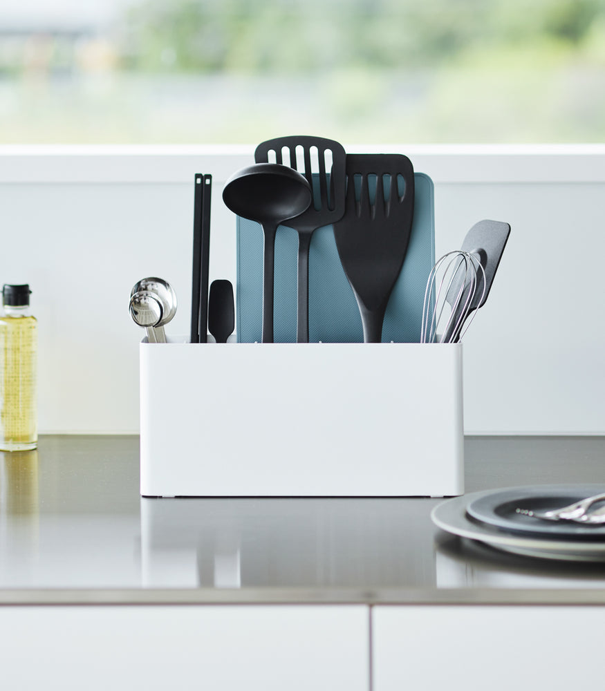 View 5 - White Utensil & Thin Cutting Board Holder by Yamazaki Home on a kitchen counter, holding various utensils and a cutting board.
