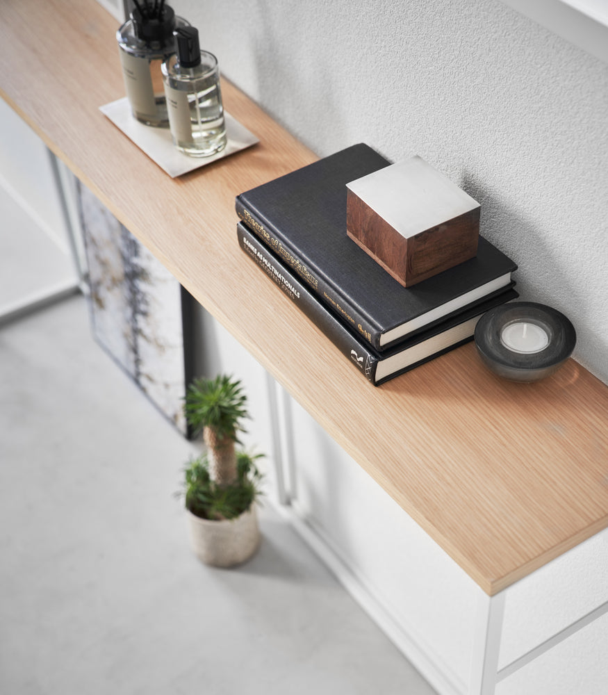 View 5 - Diagonal, close-up view of the Long Console Table by Yamazaki Home in white placed by a wall with decorative items.