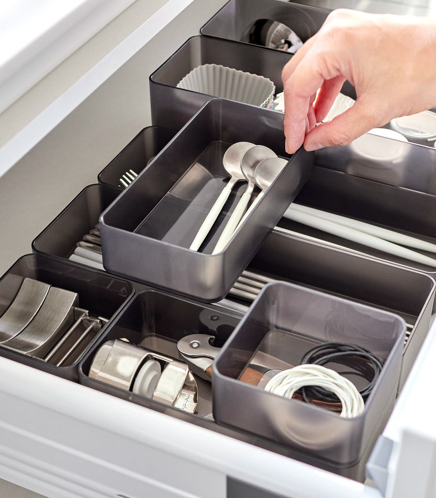 View 27 - Close-up image of four different sizes of stackable clear organizers in black—small, medium, large, and deep—neatly placed in a kitchen drawer. They effectively organize various items such as cutlery, bottle openers, and small trays, showcasing their versatility and stackability.