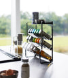 Side view of a Black Four-Tier Slim Spice Rack by Yamazaki Home neatly organized with spices and oil bottles on a light kitchen countertop.