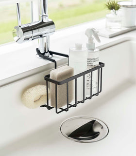 Black Faucet-Hanging Sponge Caddy attached to the kitchen sink faucet and holding sponges and cleaning supplies by Yamazaki Home. view 16