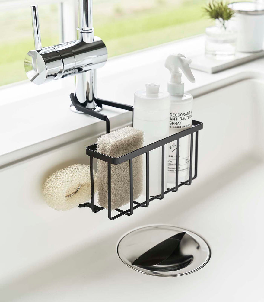 View 16 - Black Faucet-Hanging Sponge Caddy attached to the kitchen sink faucet and holding sponges and cleaning supplies by Yamazaki Home.