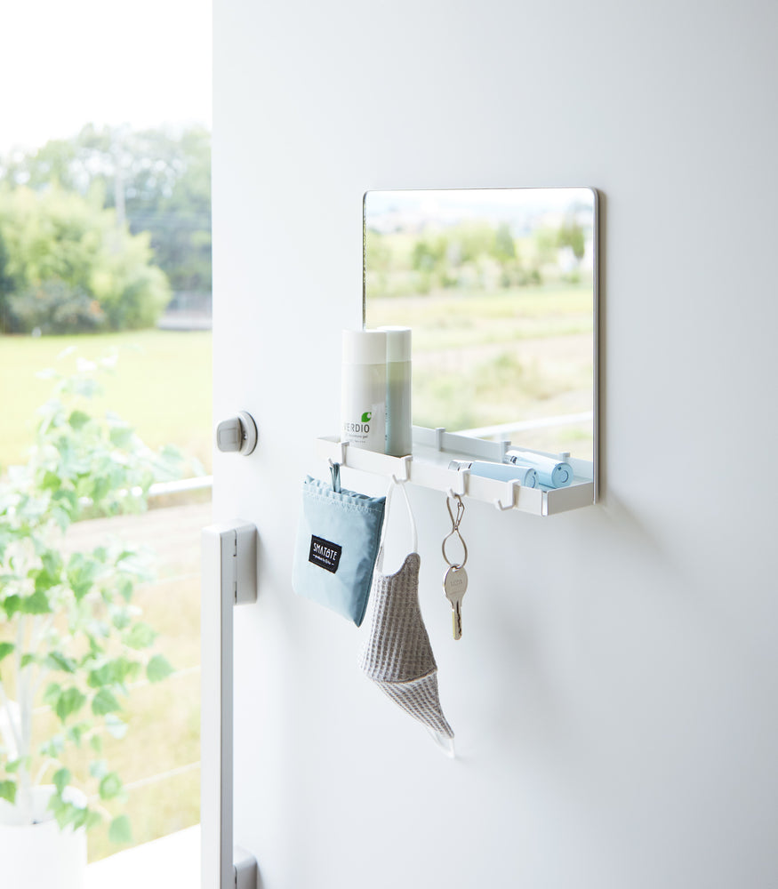 View 2 - A white Yamazaki Magnetic Mirror With Storage Rack attached to a door with a hanging bag, mask, and key.